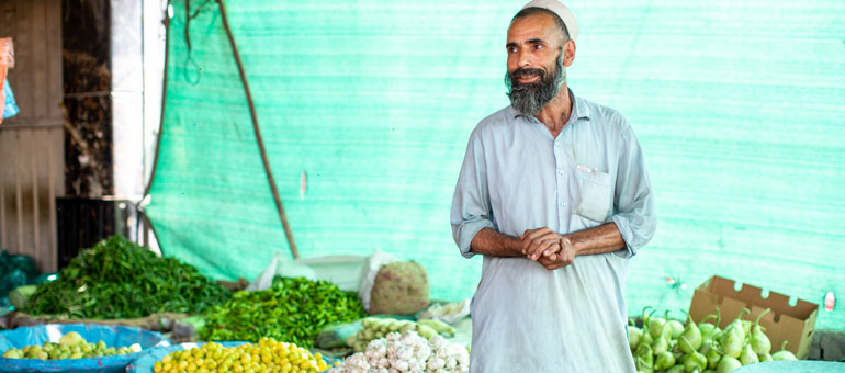 A man selling vegetables in Pakistan with a green background