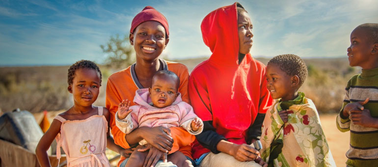 Two mothers with their children - one smiling to the camera and the other one looking away