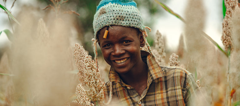 Youth in a sorghum field wearing a blue hat and smiling
