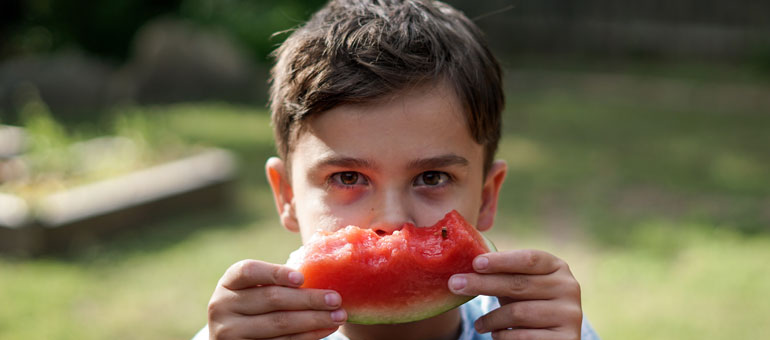 Child holding a piece of watermelon in front of his eyes