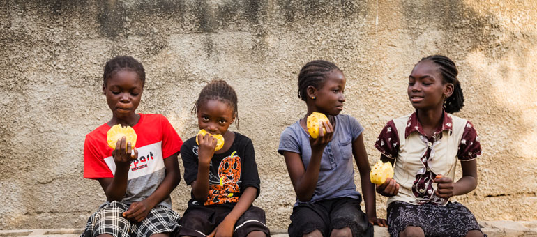 Kids sitting down on a bench and eating yellow fruits