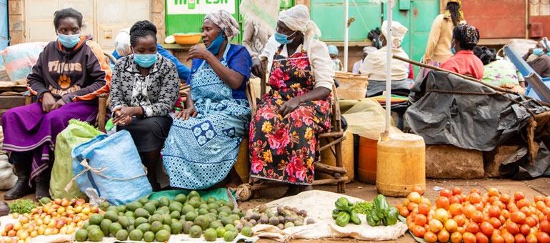 Four women sitting and talking while wearing a mask and with food at their feet