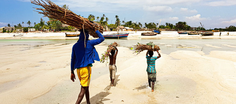 Man and two kids on the beach carrying wood on their heads