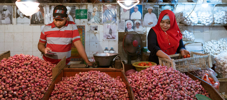man and woman in surabaya market selling onions and man looking at his phone