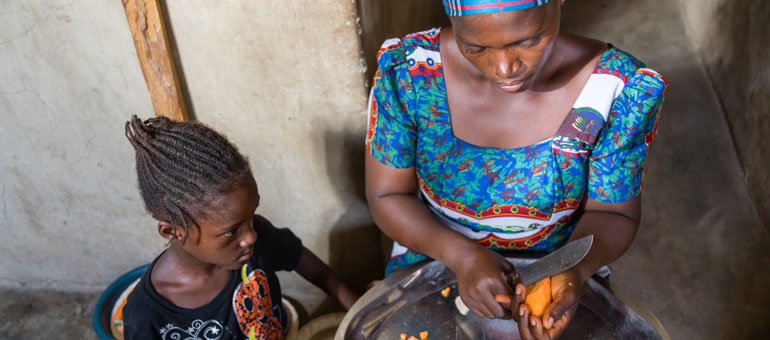 A mother cutting sweet potato and child observing