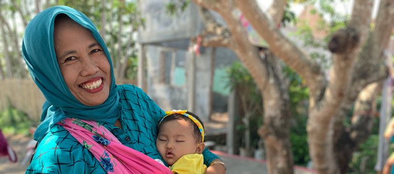 Mother holding sleeping baby and smiling in Indonesia