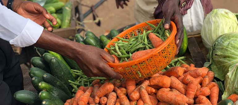 Two hands passing an orange basket of carrots and green beans