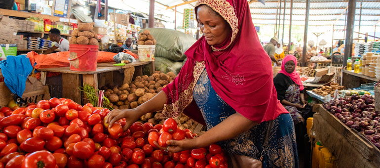Woman wearing a red veil over head picking tomatoes from a food stall