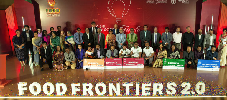 The winners of the Food Frontiers competition smiling on stage and showing the prizes
