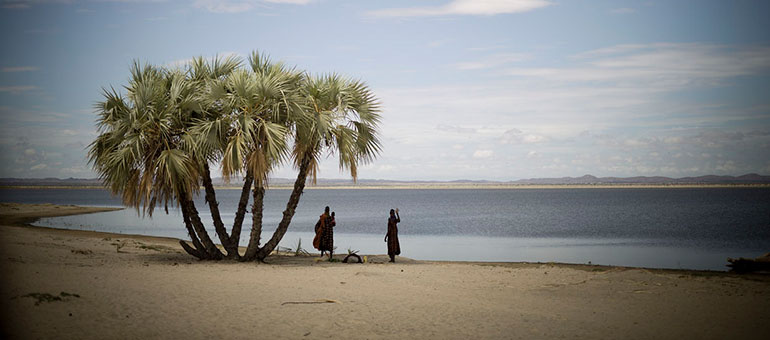 Two men waving under palm trees next to ocean in Kenya