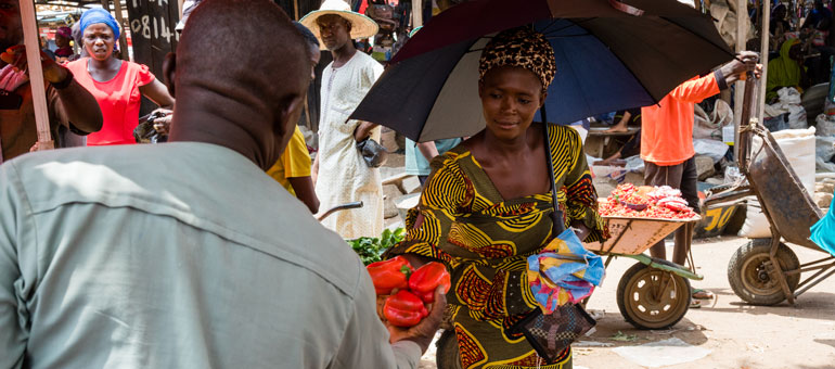 Woman buying food from a street vendor in Africa while holding the umbrella