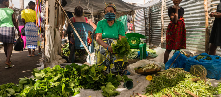 Woman in Beira market in Mozambique selling lettuce while wearing a mask