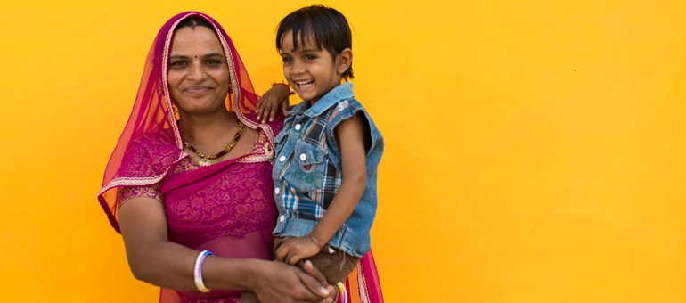 Woman wearing a purple dress and holding a boy in India against yellow background