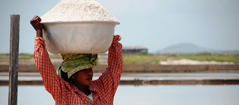 Woman wearing a checked shirt carries salt on her head