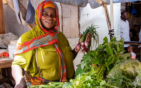 Woman at the market wearing a orange scarf smiling holding onions