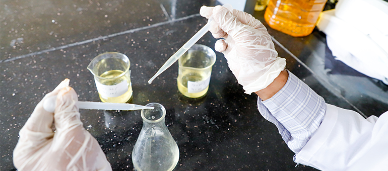 Oil being measured out and checked for fortification standards by two gloved hands