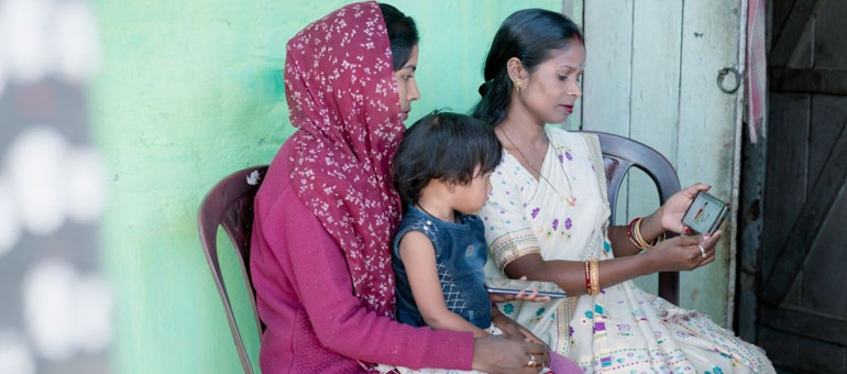 Two women sitting down with a child and looking at the phone