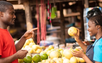African man pointing at woman holding fruit in a market