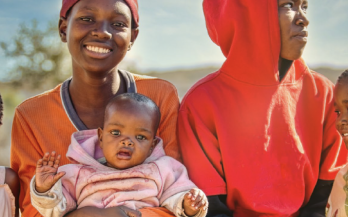 A woman and baby smile at the camera, a third adolescent looks off to the distance