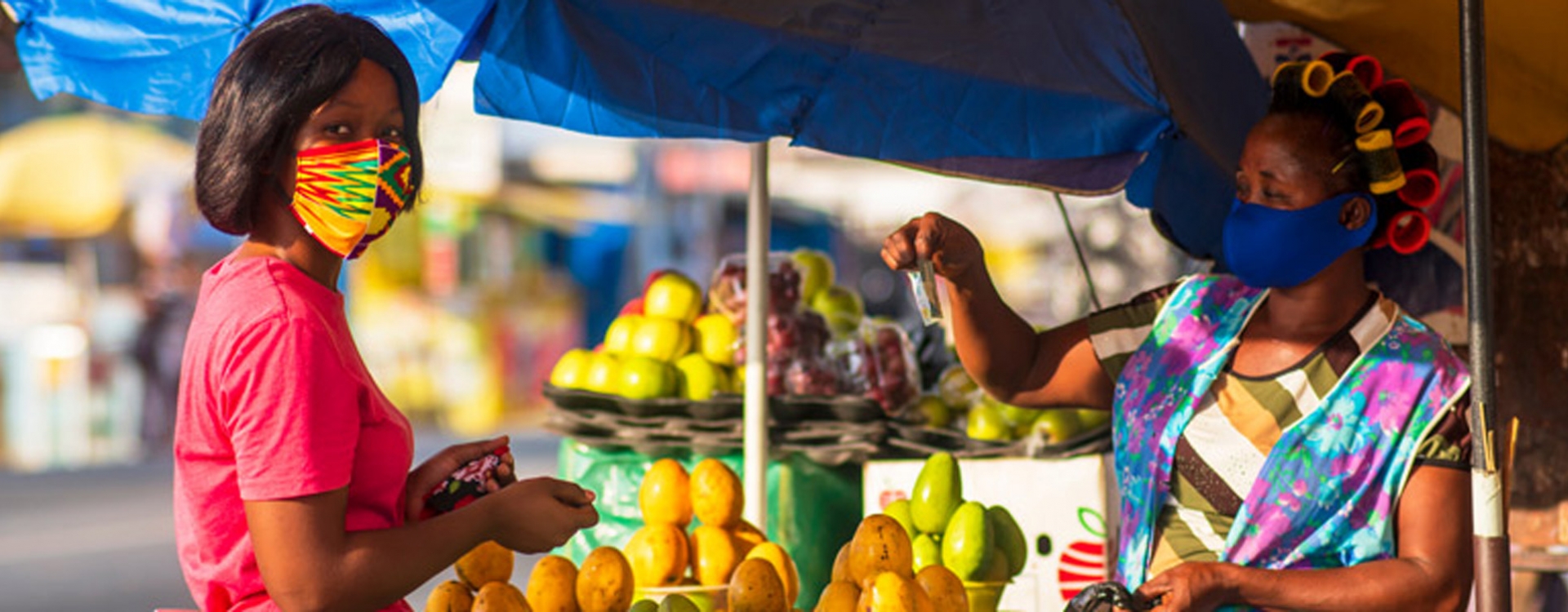 Woman buying papaya from a lady in the street while wearing a face mask