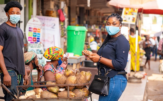 Woman buying food from guy wearing masks and looking at the camera