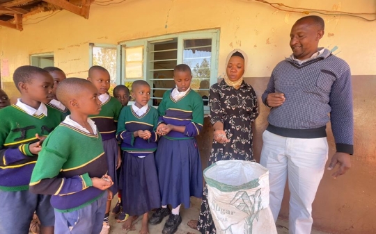 primary school kid with a bag of beans and teachers overlooking
