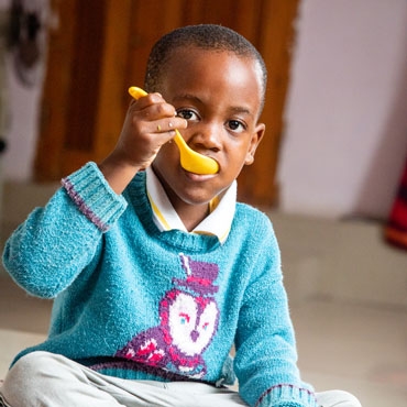 A child eating porridge with a yellow spoon