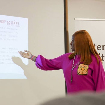 Joyce wearing a pink blouse and pointing at the screen